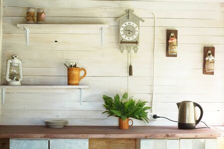 Small rustic kitchen with a clock on the wall, white plank walls and wooden shelves.の写真素材