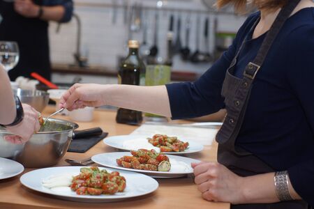 A cook in an apron sets the table, laying tomatoes in caprese salad with pesto.の写真素材