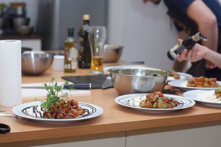 A cook in an apron sets the table for several people, laying out tomatoes in a caprese salad with pesto.の写真素材