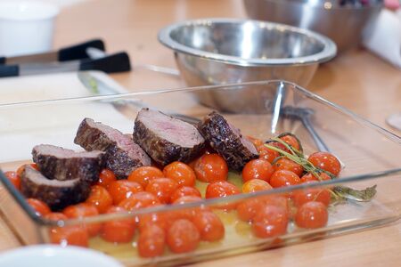Sliced beef tenderloin with baked cherry tomatoes with white sauce.の写真素材