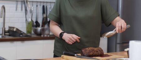 A cook with a round clock takes a beef tenderloin with tongs.の写真素材