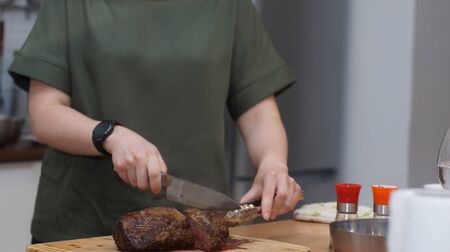 A cook with a round clock slices a baked beef tenderloin on a wooden board.の写真素材