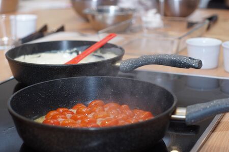 Two pans on the stove, in one cherry tomatoes, in another white sauce, steam comes from heating.の写真素材
