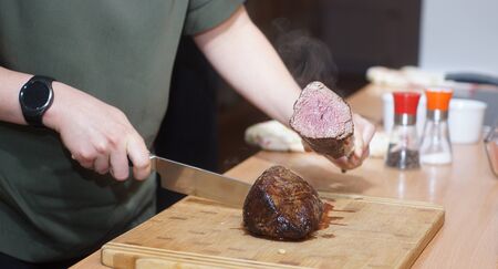 A cook with a round clock cuts a beef tenderloin and checks the readiness.の写真素材