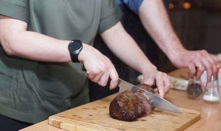 A cook with a round clock slices a beef tenderloin on a wooden board.の写真素材