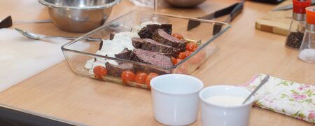 Ready-made dish with beef tenderloin, cherry tomatoes and sauce on a table in a glass patch.の写真素材
