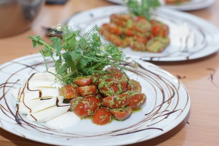 On the table is a freshly prepared caprese salad with pesto and cherry tomatoes for several people.の写真素材