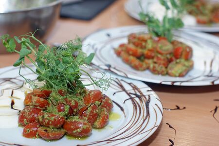 In the kitchen, a freshly prepared caprese salad with pesto and cherry tomatoes for several people.の写真素材
