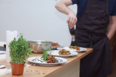 Chef in apron sets the table for several people, caprese salad with pesto sauce and herbs for decoration.の写真素材