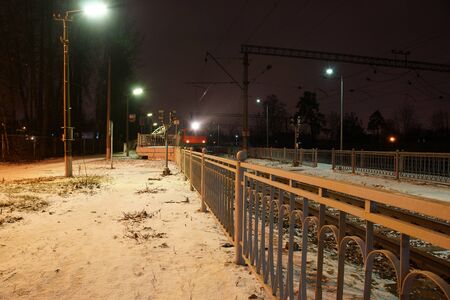 The train station at the station fenced with metal bars in the winter, the train arrived and stands on rails.の写真素材
