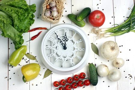 white clock with arrows lying on the boards in the middle of different vegetables for making salad.の写真素材