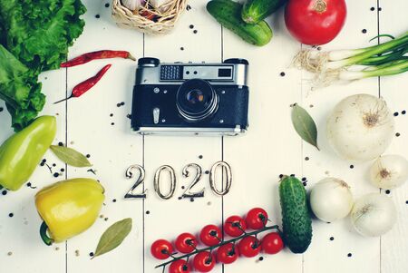 Old camera and numbers 2020 lie in the middle of bright vegetables on a white boardwalk.の写真素材