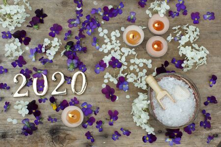 Figures 2020 on a wooden background next to the flowers of purple pansies and white bath salt, spa concept.の写真素材