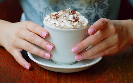 Elegant female hands with manicure hold a cup with a cream-covered drink.の写真素材