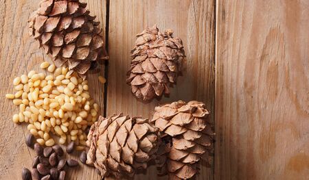 Cedar cone and pine nuts lie on a wooden table, top view.