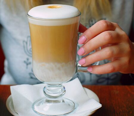 Elegant female hand hold a transparent cup with hot latte coffee in a cafe.の写真素材