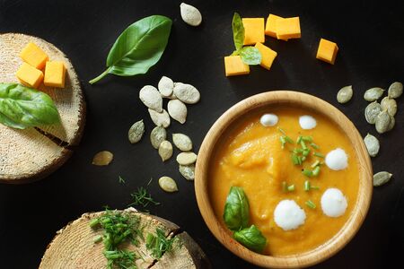 Top view of cream pumpkin soup in a bamboo bowl on a table with ingredients.の写真素材