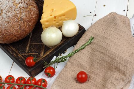 Rye bread, two onions and a sprig of cherry tomatoes lie on a wooden white table next to a beige towel, top view, copy space for your text.の写真素材