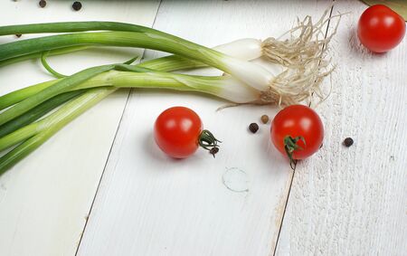 A sprig of green onion and three cherry tomatoes lie on a white wooden table.の写真素材