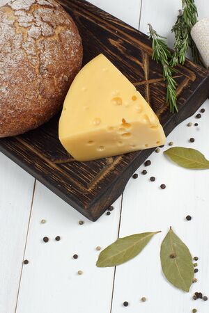 Rye bread and cheese lie on a dark board on a wooden white table, top view.の写真素材