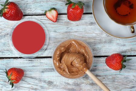 Whipped honey in a jar on a light wooden table next to red strawberries, top view.の写真素材