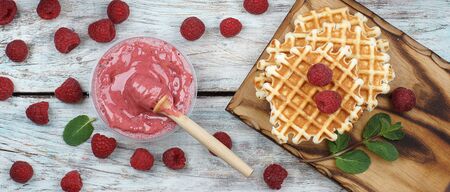 Pink whipped honey in a jar with a spindle spoon, juicy large raspberries and sweet waffles on the table, top view, panorama.の写真素材