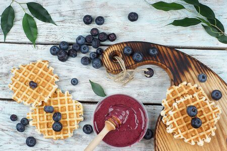 Blueberries and waffles on the table, next to whipped honey in a jar, top view.の写真素材