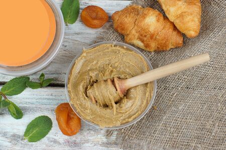 Whipped honey with apricot on a table in a jar with a spoon spindle, next to croissants, dried apricots and mint, copy space for text and product advertising on the cover.の写真素材