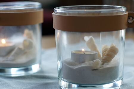 Two candles in transparent candlesticks with sand and a shell are on the table.の写真素材