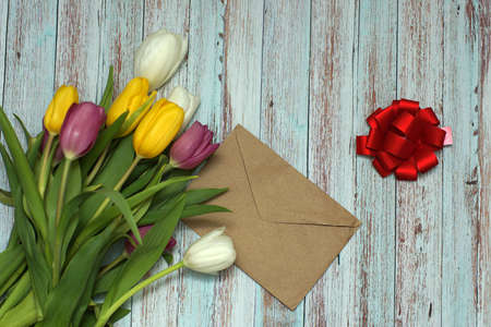 The envelope lies on a table of blue boards next to a beautiful bouquet of colorful tulips and a red bow.の写真素材