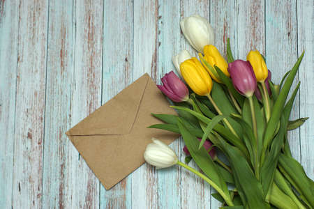 The envelope lies on a table of blue boards next to a beautiful bouquet of colorful tulips.の写真素材