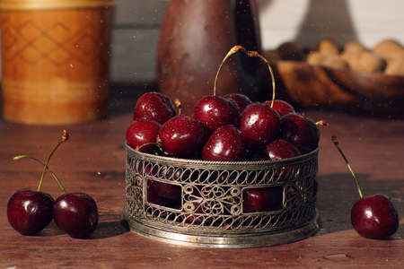 Cherry berries in a beautiful carved bowl on a table with water droplets.の写真素材