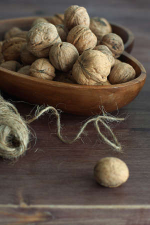 Inshell walnuts lie in a wooden dish, next to twine and a hammer for cracking nuts.
