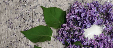 Panorama or still life with a white cosmetic product in a small bottle with a lid and lilac flowers...