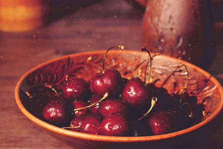 Red ripe cherries lie in a brown plate next to a brown jug on the table in the village.