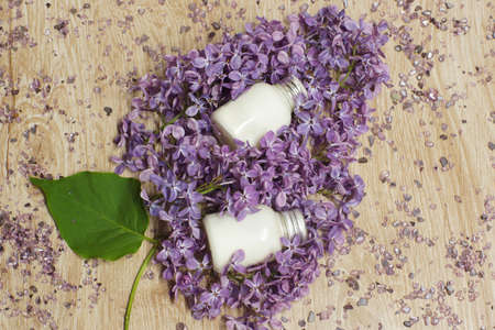 On a wooden table there is an image of a lilac branch with a bunch of flowers, which is white bottles with a cosmetic product, spa conceptの写真素材