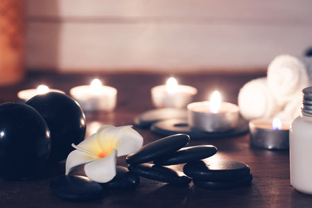Flat black hot massage stones and left plumeria flower on the table with spa set.の写真素材