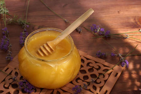 A jar of natural honey with a spindle spoon on a mat on the table next to lavender.の写真素材