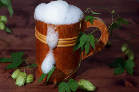 Beautiful wooden beer mug full of beer and foam on the table with hop plant.の写真素材