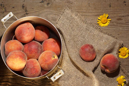 Peaches in a saucepan and small yellow flowers on the table.の写真素材