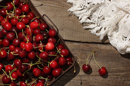 Red cherries on a tray next to white lace fabric.の写真素材