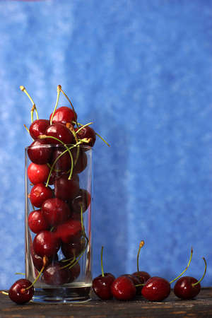 A glass with ripe cherries stands on a board near a blueの写真素材