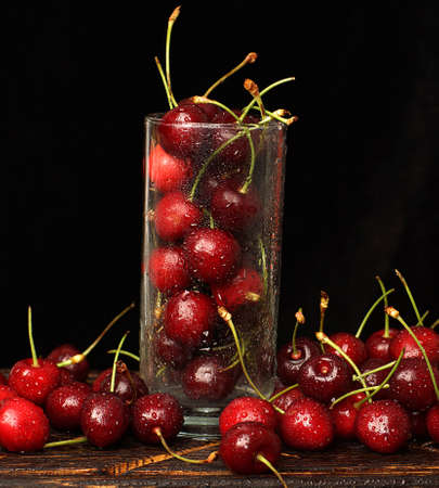 Glass with ripe cherries on a dark background with water droplets.の写真素材