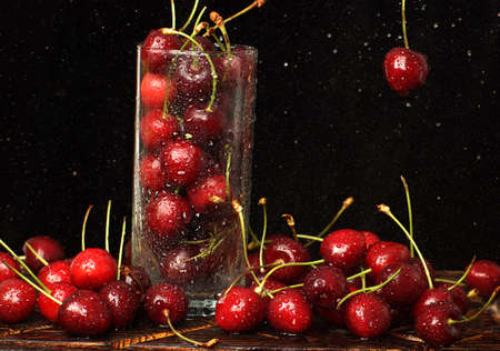 Sweet cherries in a glass on the table and hanging on a dark background.の写真素材