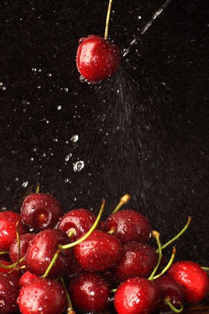 A jet of water beats into a red cherry berry on a dark background.の写真素材