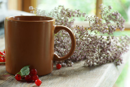 a brown ceramic mug stands on the table next to a bunch of small flowers.の写真素材