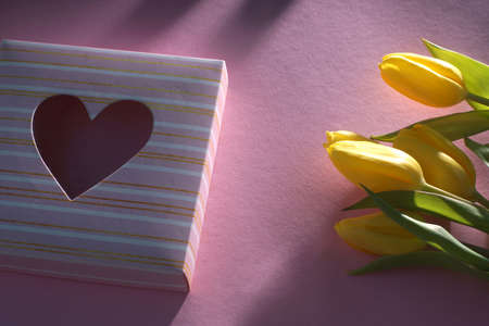 Bouquet of yellow tulips on a pink background and a box with a heart.