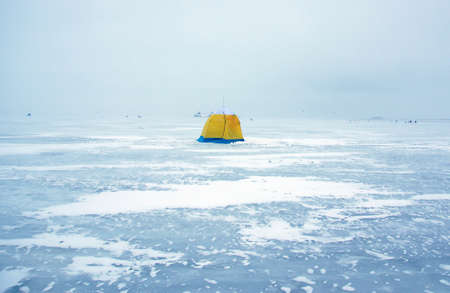 A yellow and blue tent stands in the middle of the bay on thick ice.の写真素材