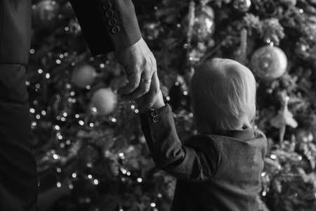 Son and father hold hands and look at the newly decorated Christmas treeの写真素材