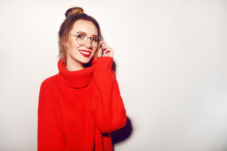 Fashion pretty cool girl wearing glasses and red sweater. Close up shot of charming female. Tender, beautiful, young. Hipster. Cute. With red lips. Happy, smile. piercing in the noseの写真素材